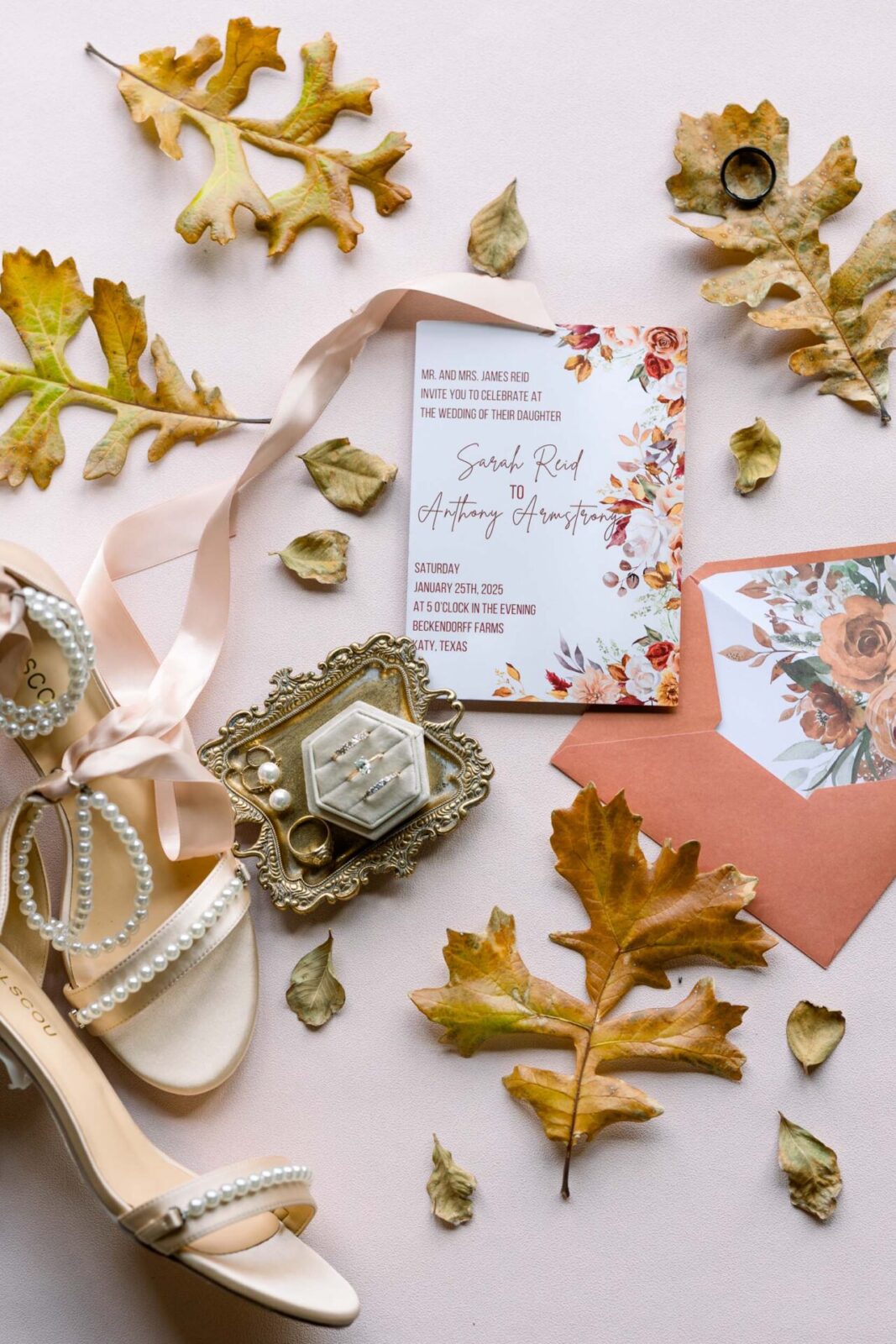 Wedding details including an invitation suite, heels, jewelry and fall leaves laid out.